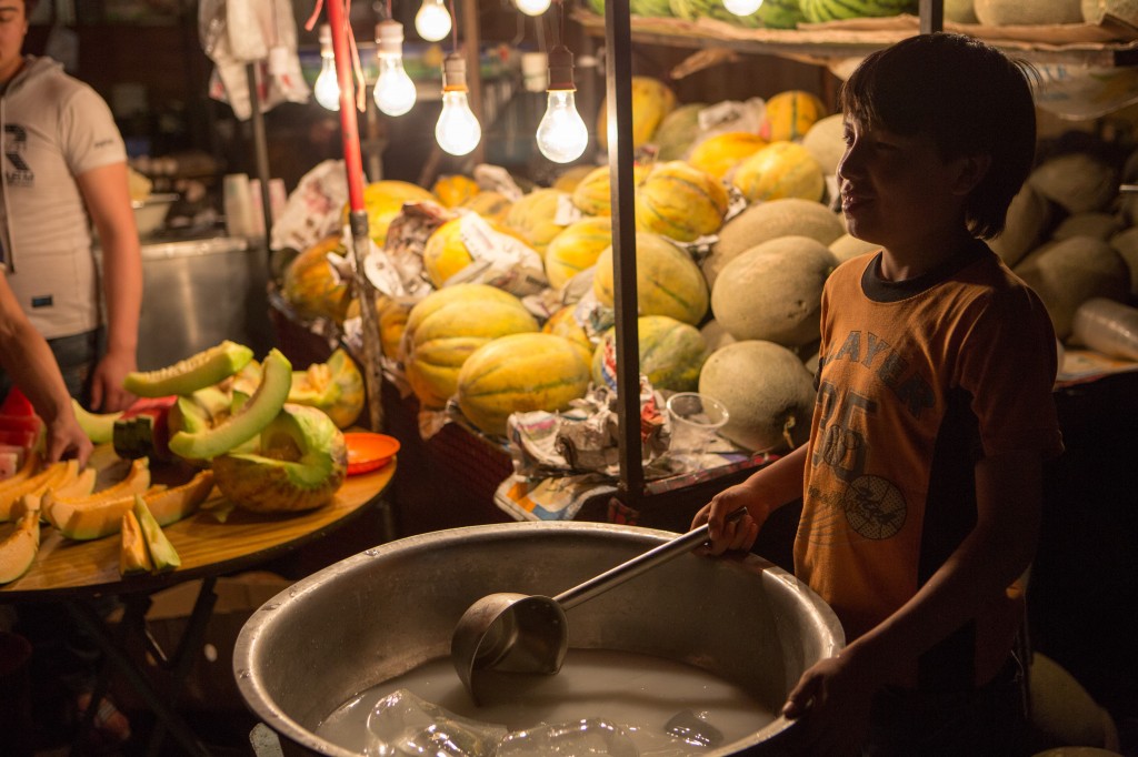 Boy selling yogurty drink beside  fruit vender