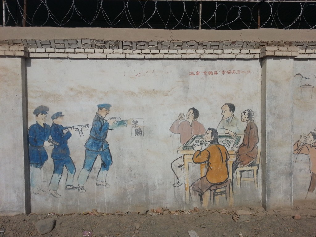In this propaganda painting, the police are barging in, guns drawn, on a group of men surreptitiously playing Mahjang. The first officer holds a sign that says, "No Gambling." In the corner above them, the caption says, "Stay far away from pornographic things, gambling and drugs, and you will live a happy and healthy life."